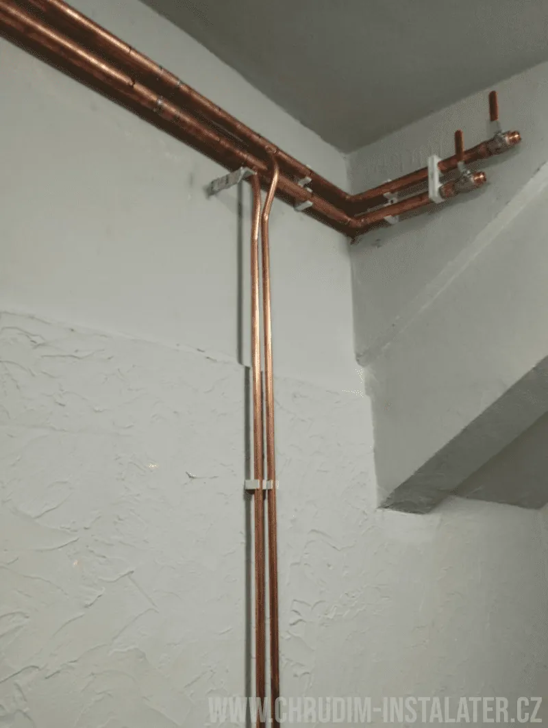 Měděné potrubí vedené pod stropem a podél stěny